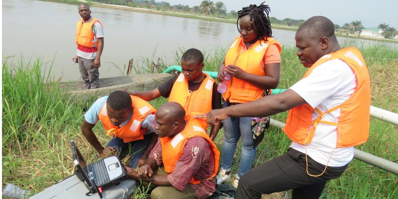 A team of researchers collecting data on a rugged laptop by a wide river