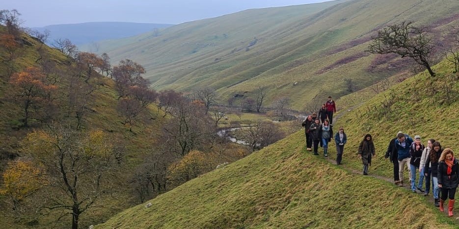A group walking along a hillside with some trees in the river valley below
