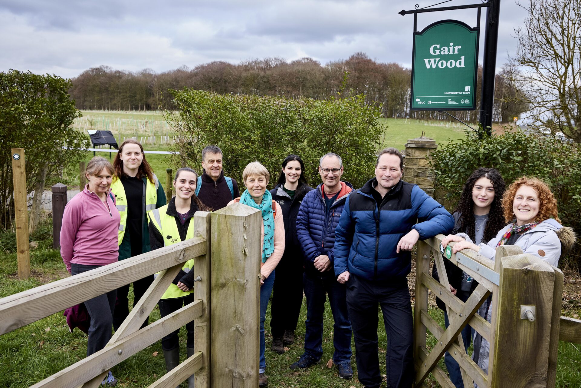 A group of people standing next to an open gate and a sign that says Gair Wood